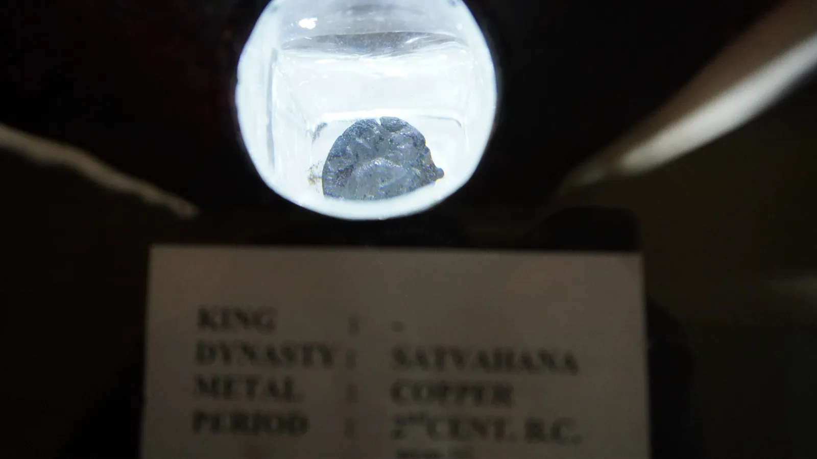 Ancient Satavahana copper coin under a magnifier, labelled 2nd century BC