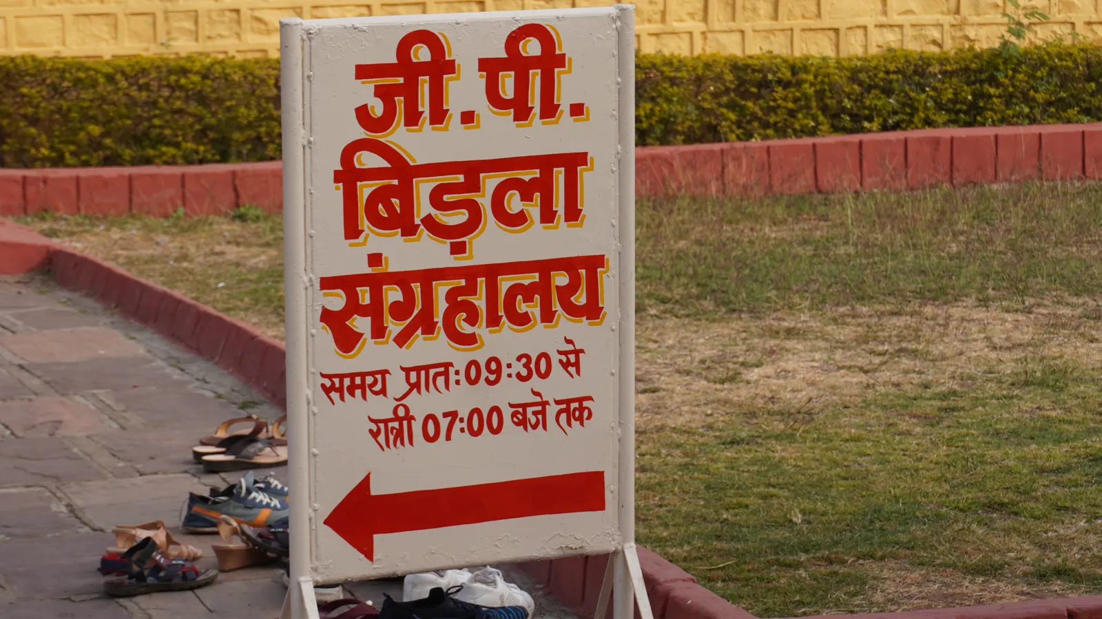 Red G.P. Birla Museum sign and arrow near the temple, with slippers left on the path
