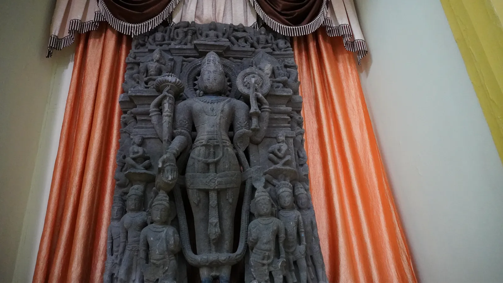 Tall grey Vishnu relief framed by orange curtains inside the Birla Museum, Bhopal
