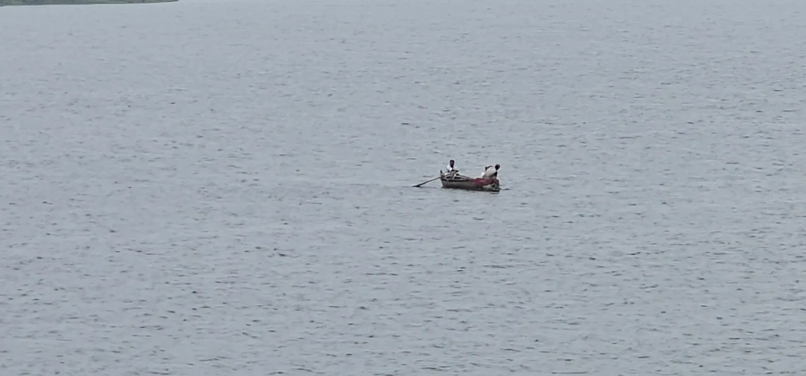 A small fishing boat far out on the calm grey water of Kaliasot Dam