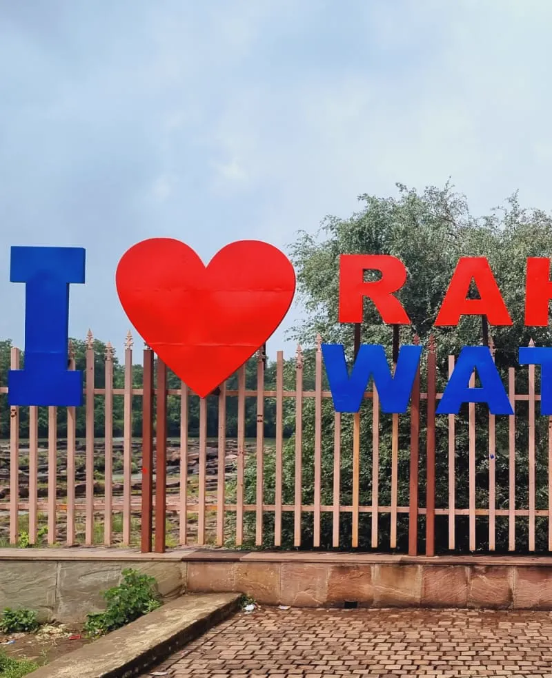 A red heart-shaped Rahatgarh Waterfall sign at the viewpoint