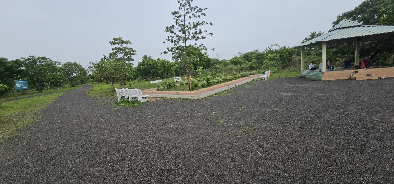 A gravel rest area with a green gazebo and white benches at Laharpur Ecological Park