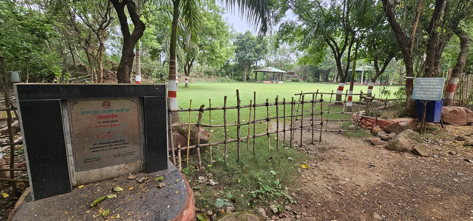 A neat green lawn ringed by trees and gazebos at Laharpur, used for yoga and morning exercise