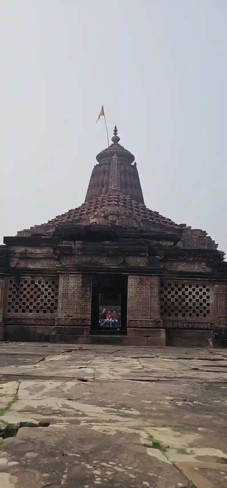 Full view of the Neelkantheshwar temple with its spire, flag and carved lattice walls