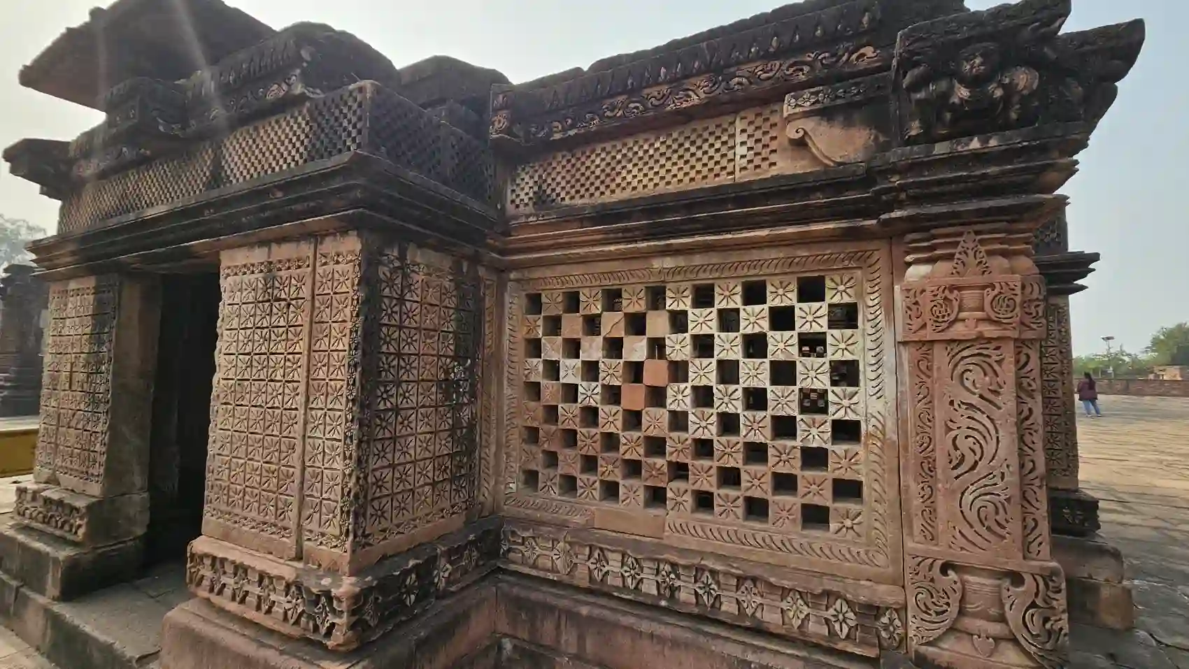 A carved checkerboard stone lattice wall on the outside of the Neelkantheshwar temple