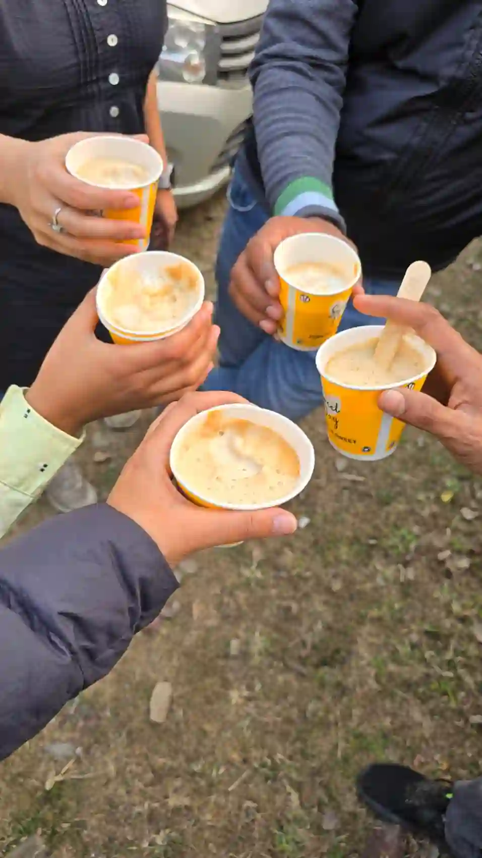 Hands raising small paper cups of fresh hot coffee among the ruins of Eran