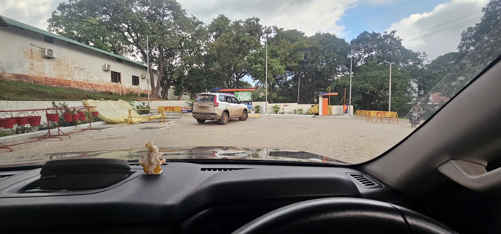 A leafy fuel-station forecourt on the edge of Pachmarhi, ringed by old trees and red hanging planters