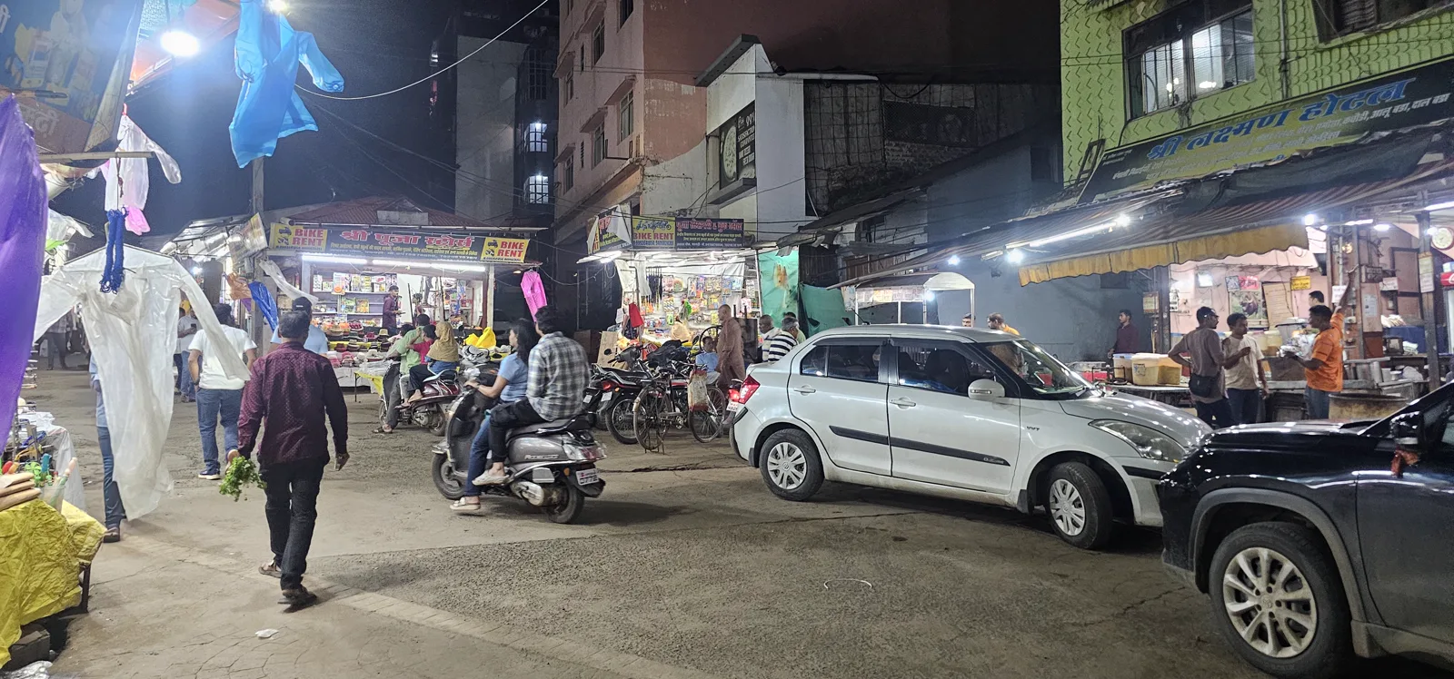 A busy Pachmarhi market lane at night with bike-rent stalls, shops and parked cars before the marathon