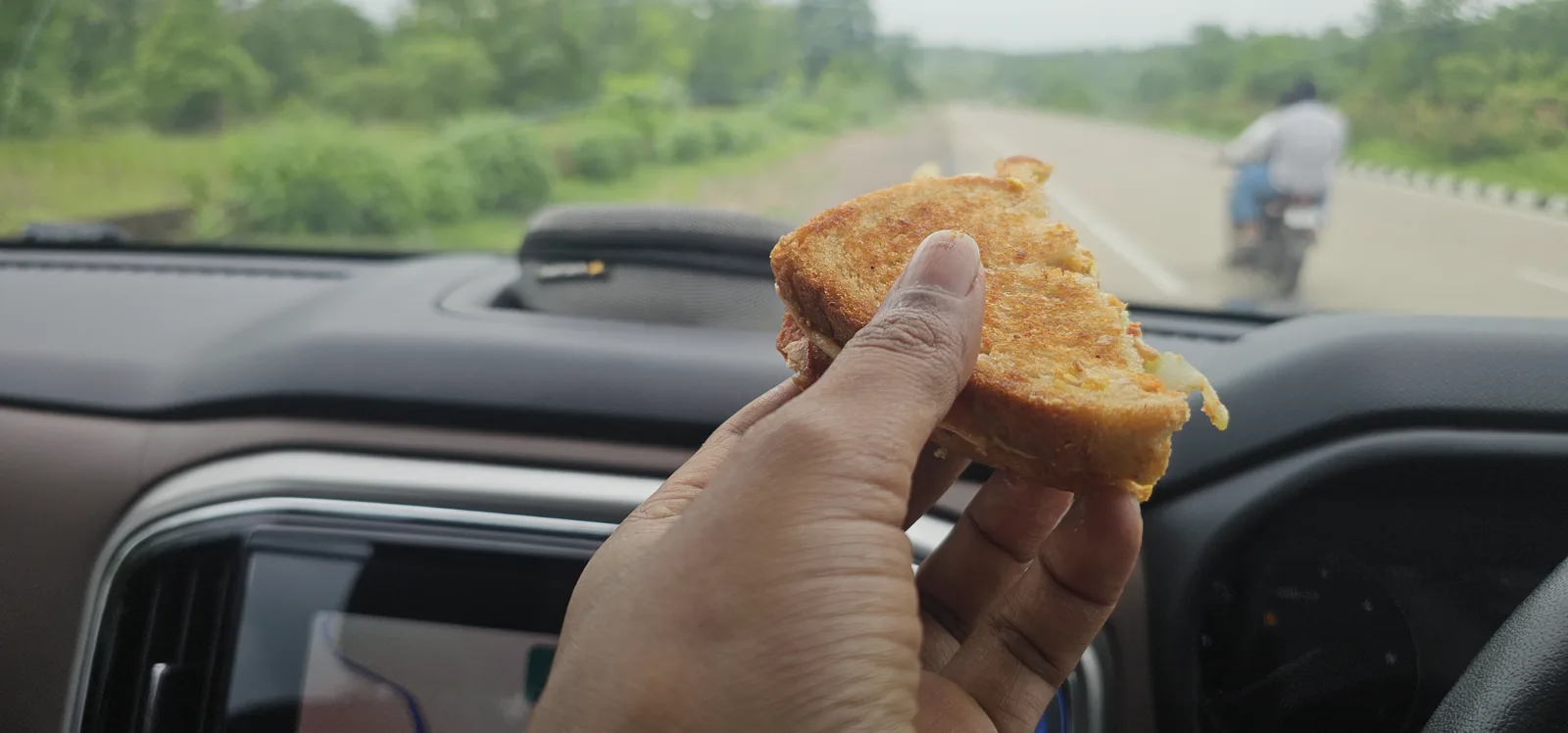 A homemade sandwich held up at the wheel on the Bhopal to Pachmarhi drive — race-weekend lunch from home