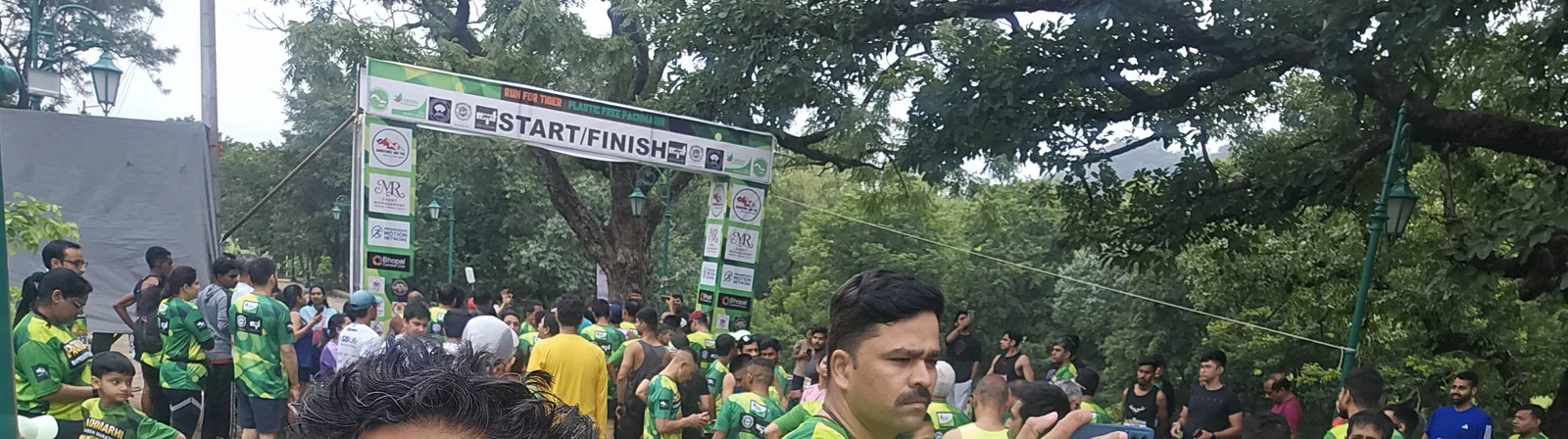 The START/FINISH arch of the Pachmarhi Monsoon Marathon 2026 with hundreds of runners in green jerseys gathering under it in the morning mist